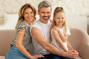 A smiling family shows their bare arms with bandages on their vaccination sites