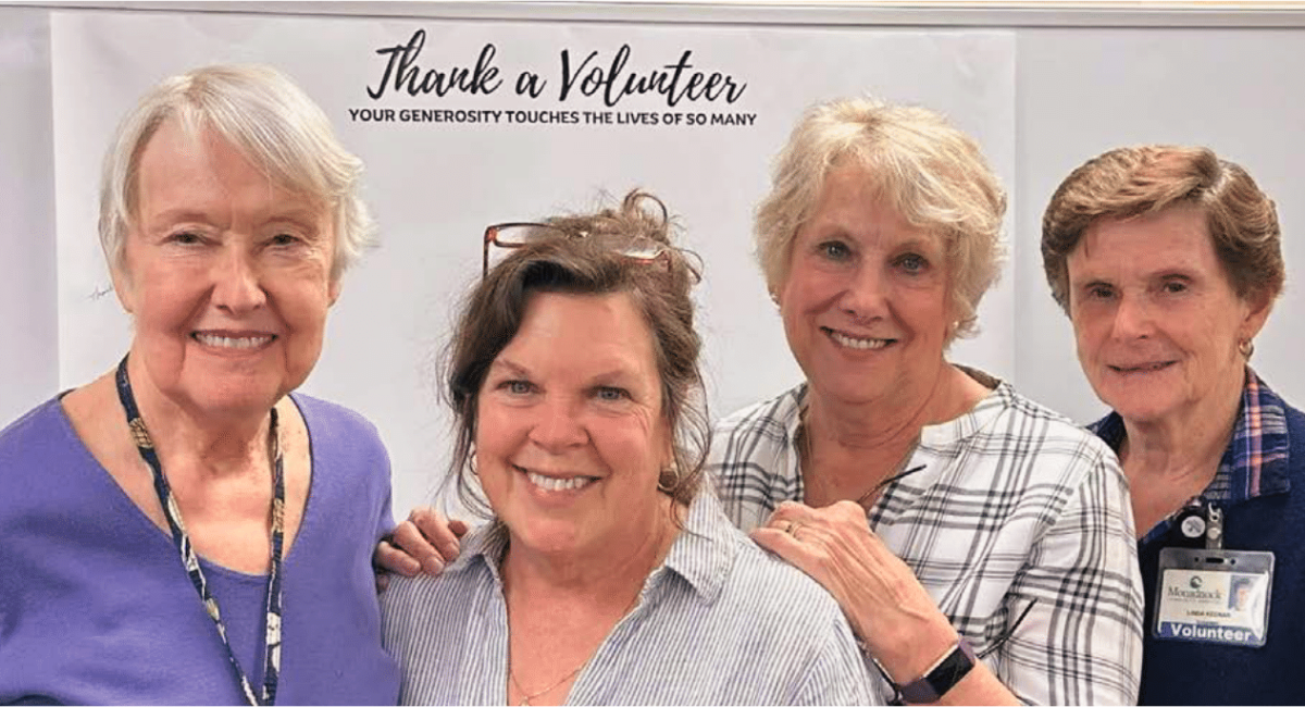 Four dedicated volunteers at Monadnock Community Hospital stand together, smiling in front of a "Thank a Volunteer" sign. From left to right: Gwyn Baldwin, Toni Gildone (Volunteer Coordinator and Window Shop Manager), Carole Connor, and Linda Keenan. Their camaraderie and commitment exemplify the spirit of volunteerism at MCH.