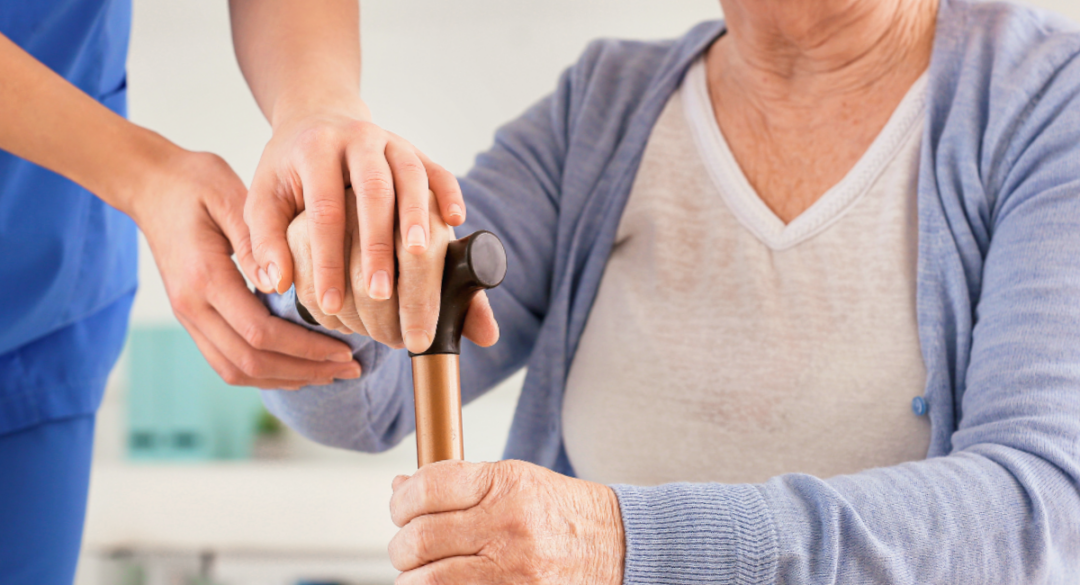 Close-up of a caregiver's hand gently supporting an elderly person holding a walking cane, symbolizing care and support for individuals with mobility challenges