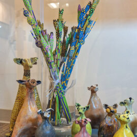 Ceramic animal figures in earthy tones with a vase of colorful decorative floral stems, adding a whimsical touch to the glass display.