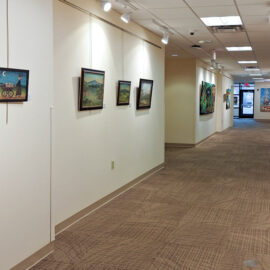 A hospital hallway decorated with framed paintings, some depicting whimsical scenes with animals. The arrangement of art along the corridor creates a warm, welcoming experience for visitors.