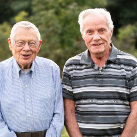 Norm Makechnie and Brad Farnham, MCH volunteers, smiling outdoors as they celebrate their 90th birthdays