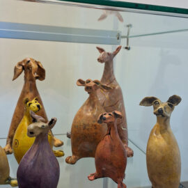 A close-up view of handcrafted ceramic animals with unique expressions and colorful designs, displayed on a glass shelf.