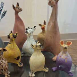 A close-up view of handcrafted ceramic animals with unique expressions and colorful designs, displayed on a glass shelf.