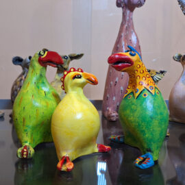 Two brightly colored ceramic bird figures with intricate patterns, surrounded by other animal sculptures with detailed designs.