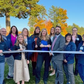 A ribbon-cutting ceremony at the Cardiology Department open house, featuring team members standing outside with a scenic autumn backdrop