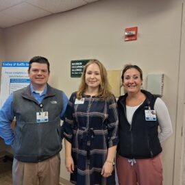 Three healthcare professionals from the Quality Department pose near a poster display, promoting engagement in the Quality Showcase event