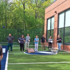 A lively cornhole competition on the newly opened turf, with participants and spectators enjoying the outdoor activity