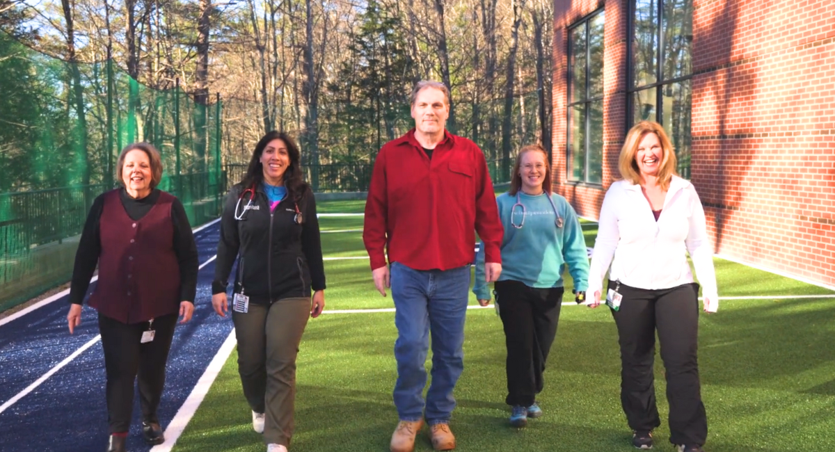 Bruce walks confidently alongside Monadnock Community Hospital's Pulmonary Rehab team on a sunny outdoor track, showcasing the transformative impact of the program.