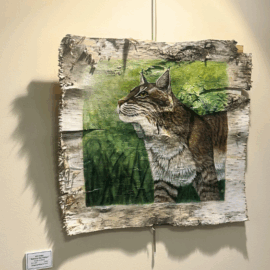 A detailed painting of a lynx on a piece of birch bark, framed by colorful origami paper cranes, part of the Birds of a Feather exhibition at MCH’s Healing Arts Gallery.