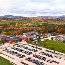 An aerial view of Monadnock Community Hospital surrounded by vibrant fall foliage, with Mount Monadnock visible in the background. The image showcases the hospital campus, parking lots, and nearby green spaces, emphasizing its picturesque location and community-oriented design