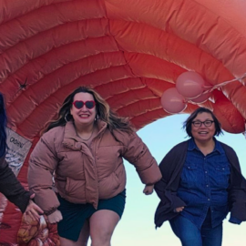 Three women energetically running through a life-sized inflatable colon model, smiling and showcasing enthusiasm for health education and community engagement