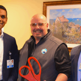 Three individuals standing together at a gastroenterology open house event, holding oversized ceremonial scissors and smiling warmly in a friendly and professional setting