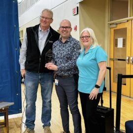 Sean Burke, Joshua Patrick, and Karen Bednarski posing together while holding the Monadnock Community Health Impact Award at the Keene Family YMCA during the "For the Health of It!" community health fair