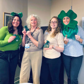 Four Monadnock Community Hospital employees from the Employee Resilience Committee (ERC) dressed in green and festive attire for St. Patrick’s Day, holding small green gift bags and gold coins