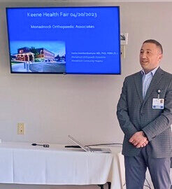 Dr. Vache Hambardzumyan presenting at the Keene Health Fair on 04/20/2023, with a screen displaying "Monadnock Orthopaedic Associates.