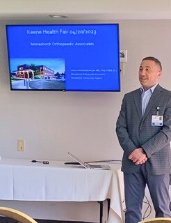 Dr. Vache Hambardzumyan presenting at the Keene Health Fair on 04/20/2023, with a screen displaying "Monadnock Orthopaedic Associates.