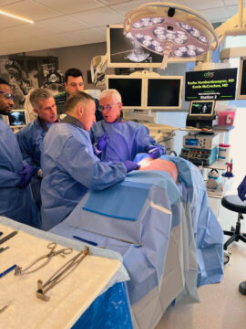 Dr. Vache Hambardzumyan performing surgery with a team of medical professionals, surrounded by surgical instruments and equipment, with monitors displaying patient information