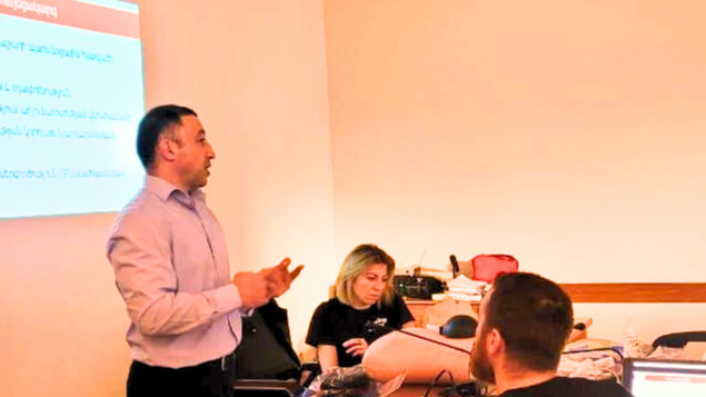 Dr. Vache Hambardzumyan speaking to a group of doctors, with a presentation projected on the wall behind him