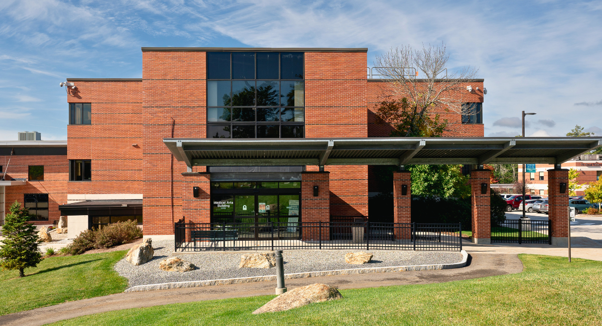 A brick building with large windows, labeled "Medical Arts Building," featuring a covered entrance with a metal canopy and a surrounding landscaped area.