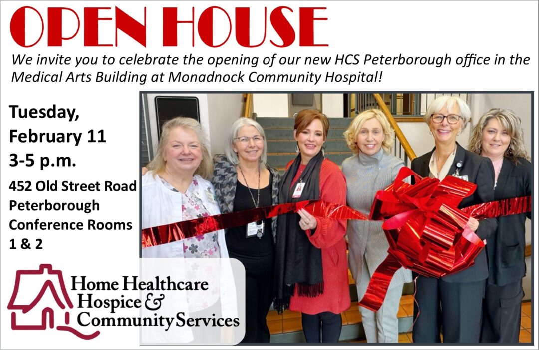Group of six individuals smiling during a ribbon-cutting ceremony for the opening of the HCS Peterborough office in the Medical Arts Building at Monadnock Community Hospital. They are standing indoors in front of a staircase, holding a large red ribbon tied into a bow. The logo of Home Healthcare, Hospice & Community Services is displayed in the lower-left corner