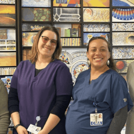 Four women standing in front of a colorful mosaic artwork. From left to right: Sherry Olson, Deiana Gaudette, Brianna Blake, and Cynthia McGuire. All are smiling and wearing professional attire.