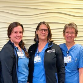 Pictured are MCH Birthing Suite nurses standing together in front of a textured wall. From left to right: Rebecca Lapinsky, Beth LeClair, Jennifer White, Trish Harper-Lentricchia, and Leah Hakala. They are dressed in blue scrubs, with some wearing black jackets, all smiling at the camera