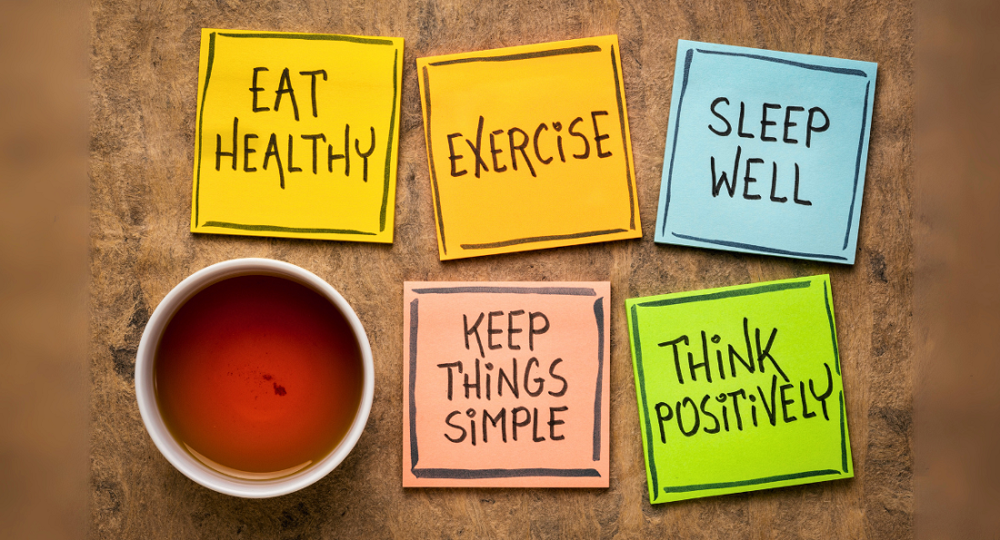 A cup of tea sits on a wooden surface next to five colorful sticky notes with handwritten wellness reminders. The notes read: "Eat Healthy" (yellow), "Exercise" (orange), "Sleep Well" (blue), "Keep Things Simple" (peach), and "Think Positively" (green).