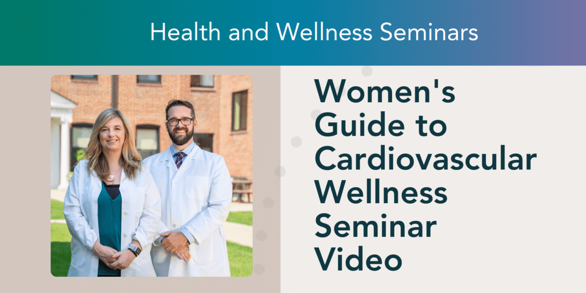 A promotional graphic for the Women's Guide to Cardiovascular Wellness Seminar Video. The image features a woman and a man, both in white lab coats, standing outdoors in front of a brick building. The woman has long blonde hair and is wearing a teal blouse, while the man has short dark hair, a beard, and glasses. The right side of the image displays the seminar title in bold blue text. The background includes a well-maintained lawn and a picnic table.