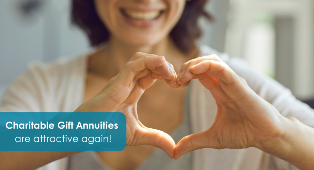 A smiling woman forms a heart shape with her hands in front of her chest, symbolizing generosity and care. The text overlay reads: “Charitable Gift Annuities are attractive again!” highlighting renewed interest in charitable giving options.