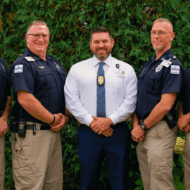 Five uniformed Monadnock Community Hospital security officers stand outside alongside a hospital leader in a white shirt and tie, all smiling for the camera. The National Night Out logos appear in the top left and bottom right corners. The image promotes the upcoming event: “Save the Date! National Night Out – Tuesday, August 5th at Monadnock Community Hospital,” celebrating community partnerships with police, fire, EMS, and local residents.