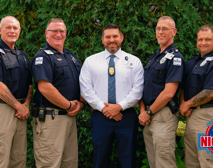 Five uniformed Monadnock Community Hospital security officers stand outside alongside a hospital leader in a white shirt and tie, all smiling for the camera. The National Night Out logos appear in the top left and bottom right corners. The image promotes the upcoming event: “Save the Date! National Night Out – Tuesday, August 5th at Monadnock Community Hospital,” celebrating community partnerships with police, fire, EMS, and local residents.