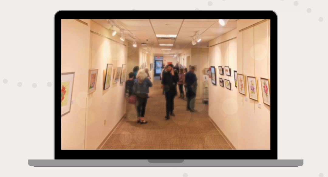 A laptop screen displaying an art exhibition in the MCH Healing Arts Gallery, with visitors viewing framed artwork along a warmly lit hallway.