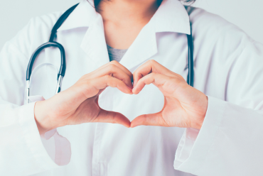 A healthcare professional in a white coat making a heart shape with their hands, symbolizing care and compassion.