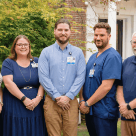 Five Monadnock Community Hospital employees stand together outside the hospital, smiling and wearing professional attire, representing gratitude for staff, volunteers, donors, and the community.