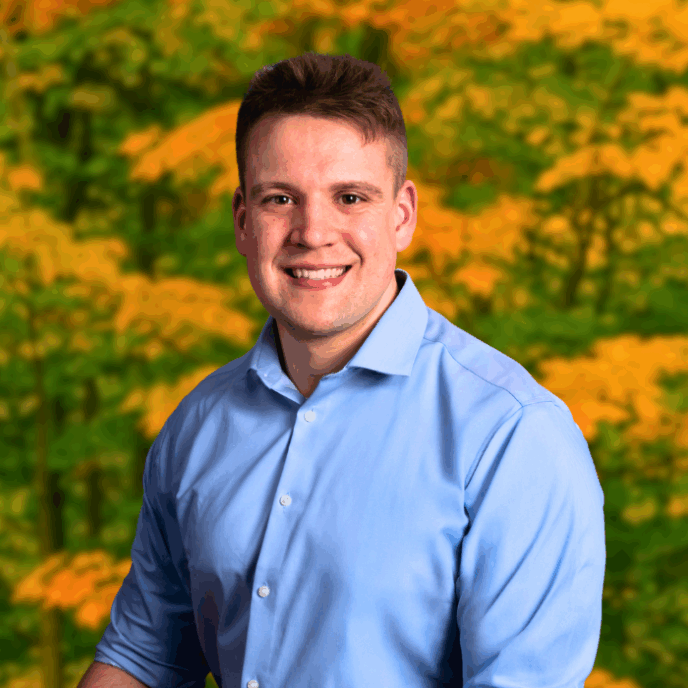 Smiling man in blue shirt standing in front of red and yellow foliage.