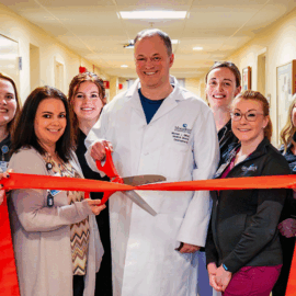 Dr. Michael Gilbert and the Monadnock Gastroenterology Associates team pose in a hallway with a red ribbon, celebrating their practice opening.smiling in a hallway.