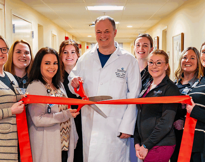 Dr. Michael Gilbert and the Monadnock Gastroenterology Associates team pose in a hallway with a red ribbon, celebrating their practice opening.smiling in a hallway.