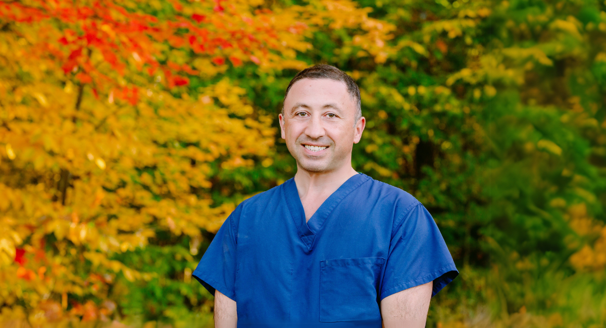 Dr. Vache Hambardzumyan, orthopaedic surgeon at Monadnock Community Hospital, smiling outdoors in front of vibrant autumn foliage.