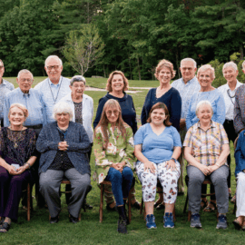 A group photo of Monadnock Community Hospital volunteers, seated and standing on a lawn with trees in the background, smiling warmly at the camera.