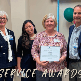 Four Monadnock Community Hospital employees smile during a 30 Years of Service Award celebration. One woman holds a certificate recognizing her for 30 years of service. Colorful balloons and a congratulatory banner decorate the background.