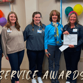 Six Monadnock Community Hospital staff members gather to celebrate a 30-year service milestone. A woman in black holds a framed certificate, surrounded by colleagues and leadership. The room is decorated with balloons and festive touches.