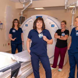 Four members of the Monadnock Community Hospital imaging team pose together in front of a CT scanner, showcasing teamwork and technology.