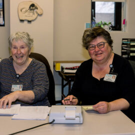 Two staff members smile while doing paperwork in an office setting.