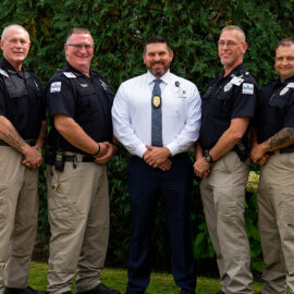 Five members of the Monadnock Community Hospital security team pose outdoors in front of green landscaping. Four wear black security uniforms, and the fifth wears a white shirt and tie with a badge.