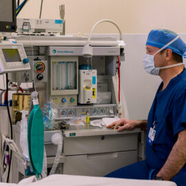A surgical staff member at Monadnock Community Hospital sits beside a fully equipped anesthesia machine in an operating room, focused and ready for the procedure ahead.
