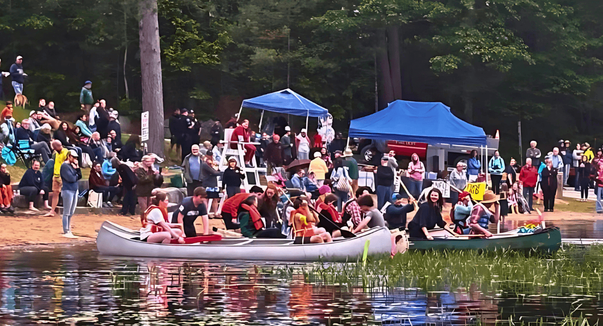 Crowds line the shore of Norway Pond in Hancock, NH, cheering on costumed teams preparing to launch canoes during the Blindfolded Boat Race to support Avenue A Teen Center. Photo by David Allen.