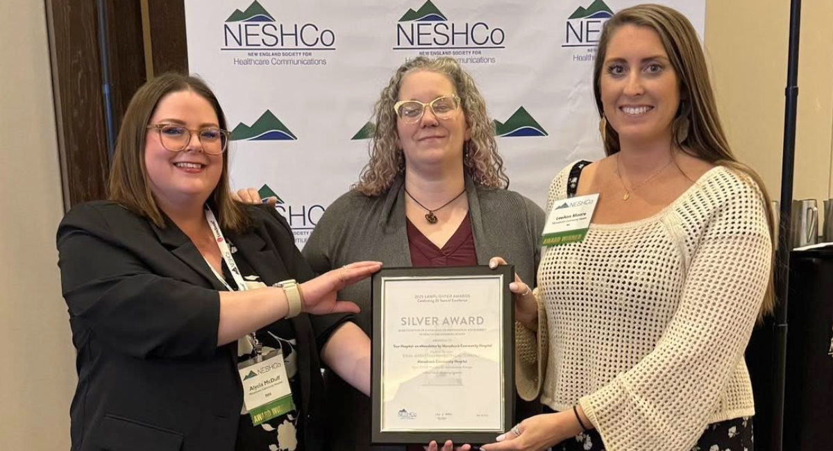 Three Monadnock Community Hospital staff members smile and proudly hold a framed Silver Award certificate in front of a NESHCo (New England Society for Healthcare Communications) backdrop, celebrating their Lamplighter Award win for the “Your Hospital” eNewsletter.