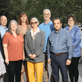 A group of 11 professionally dressed adults standing outdoors on a paved walkway, posing for a photo with trees and buildings in the background. The group includes Dr. Shawn Harrington, seen in a blue shirt and khaki pants near the rear center.