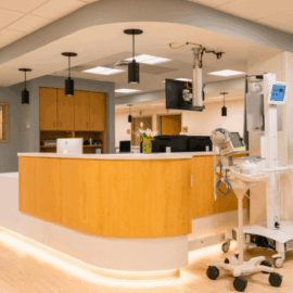 A brightly lit nurses’ station at Monadnock Community Hospital with curved wood paneling, modern pendant lights, and mobile medical equipment nearby.